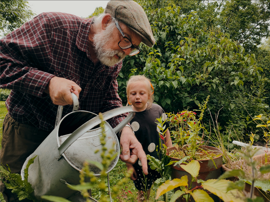 old man teaches girl about plant in garden
